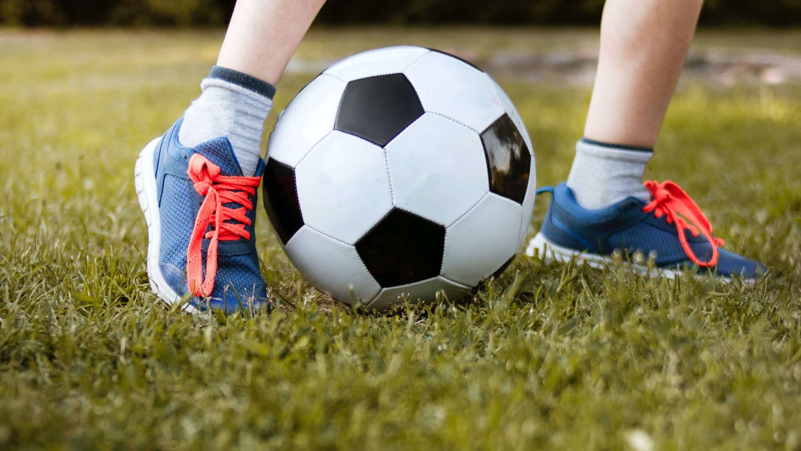 רגליים של ילד עם כדור רגל על מגרש דשא.